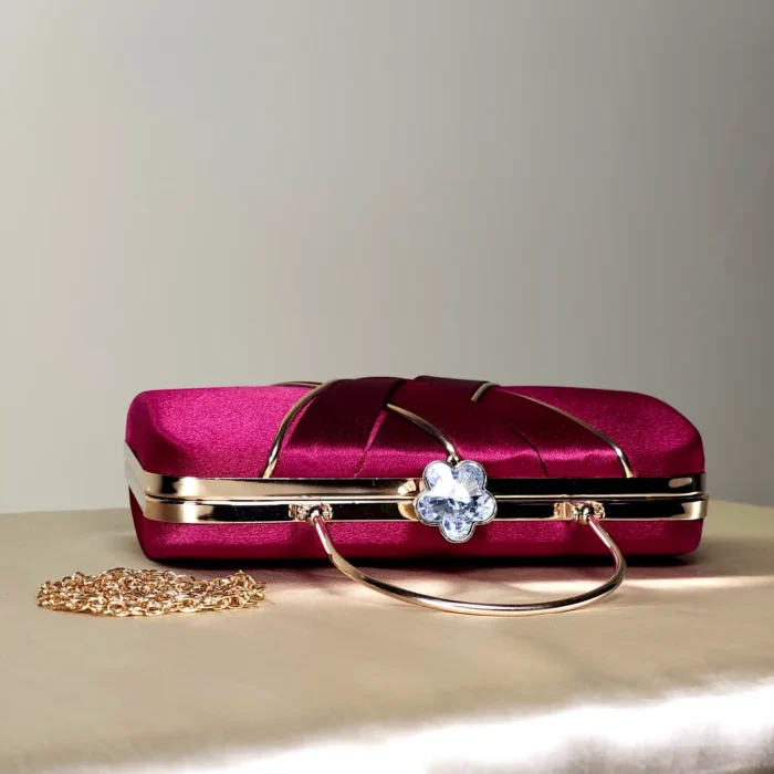Compact structured maroon clutch bag with decorative overlapping front detailing and a sleek top handle