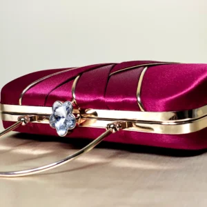 IMG_20260820_144859 Compact structured maroon clutch bag with decorative overlapping front detailing and a sleek top handle
